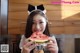 A woman in a maid outfit eating a slice of watermelon.