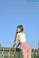 A woman in pink shorts and a white tank top posing on a bridge.