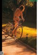 A naked woman riding a bike down a sidewalk.